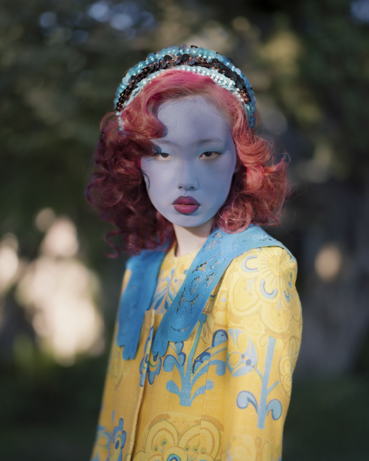 Model with blue facepaint and red lips with a red hair outside in a garden